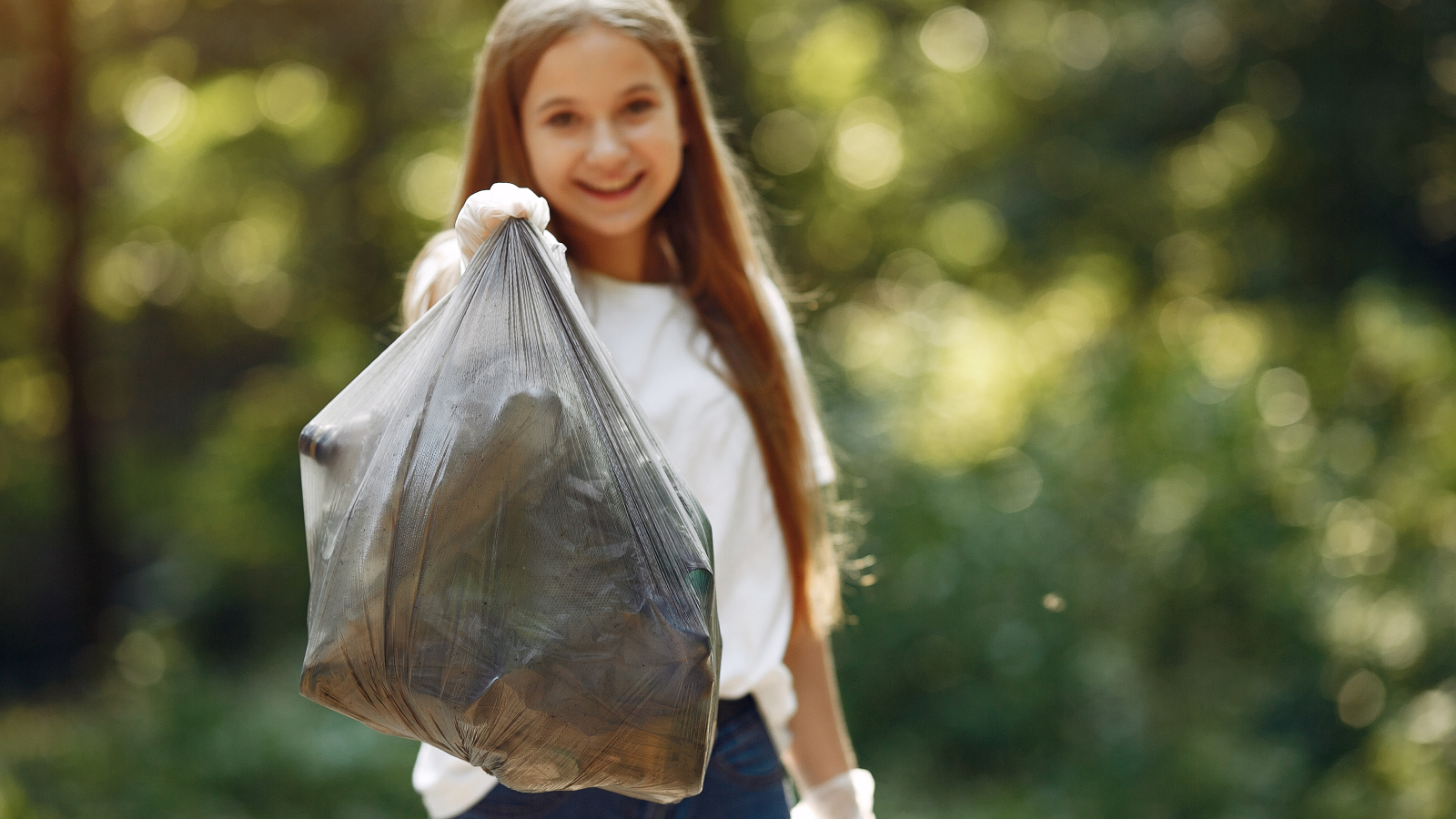 Volunteer collects rubbish. Girl in a park. Young lady in a white t-shirts